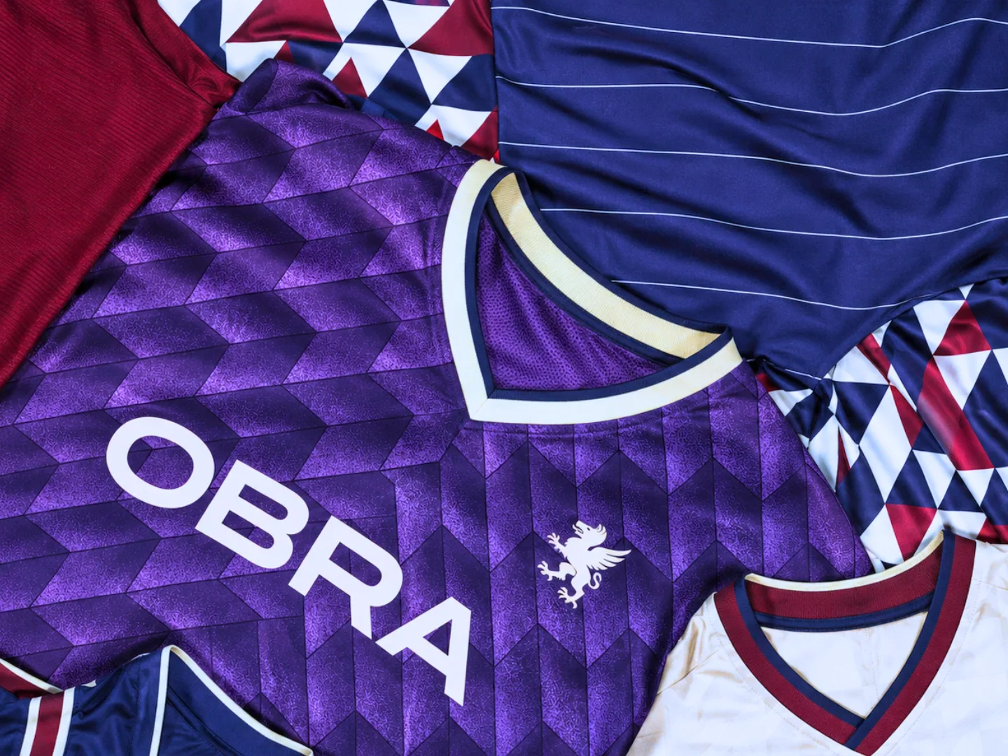 OBRA football jerseys laid flat, including a purple jacquard shirt with the OBRA wordmark and griffin crest